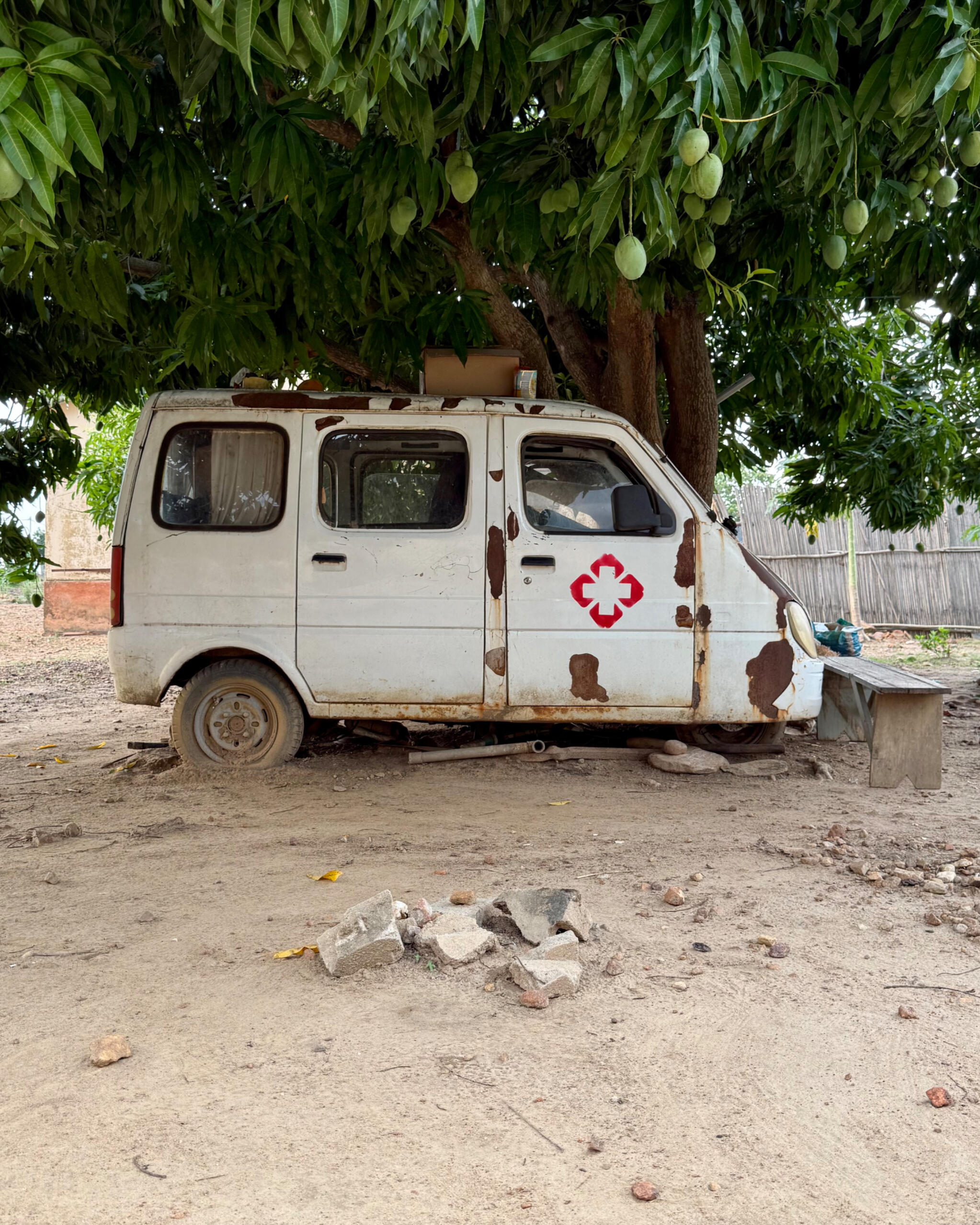 Einst funktional: Krankentransporter, aus Mangel an (Geld-)Mitteln leider stillgelegt Krankentransporter, der verrostet und kaputt vor einem Mangobaum steht